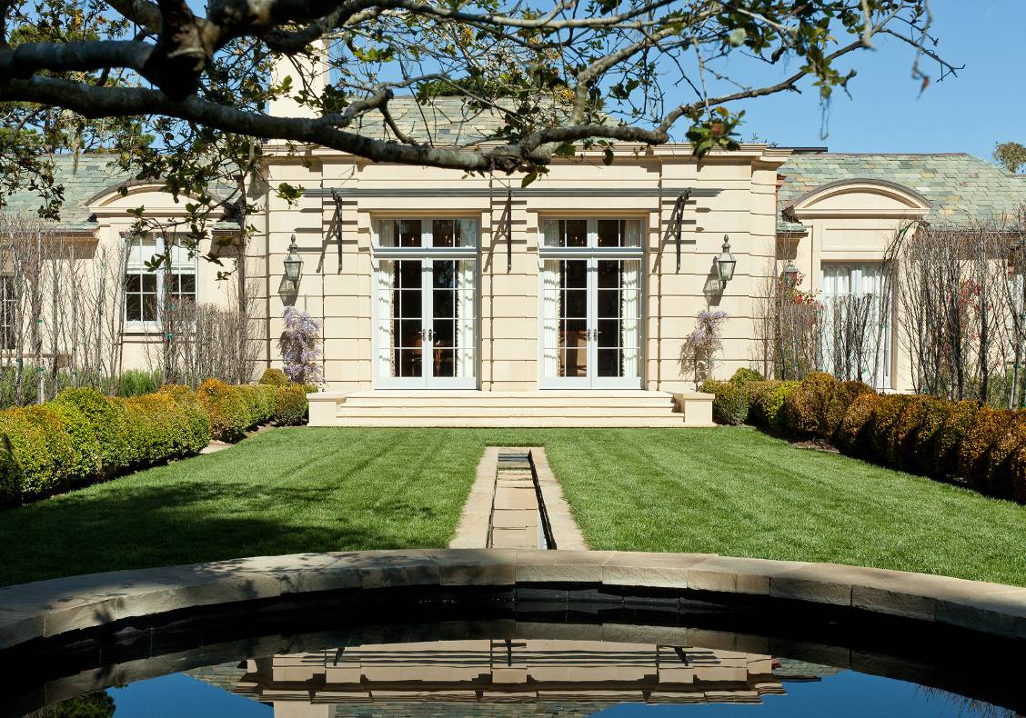 The paired French doors of the library face the lawn and a stone-bordered rill leading to a circular fountain.